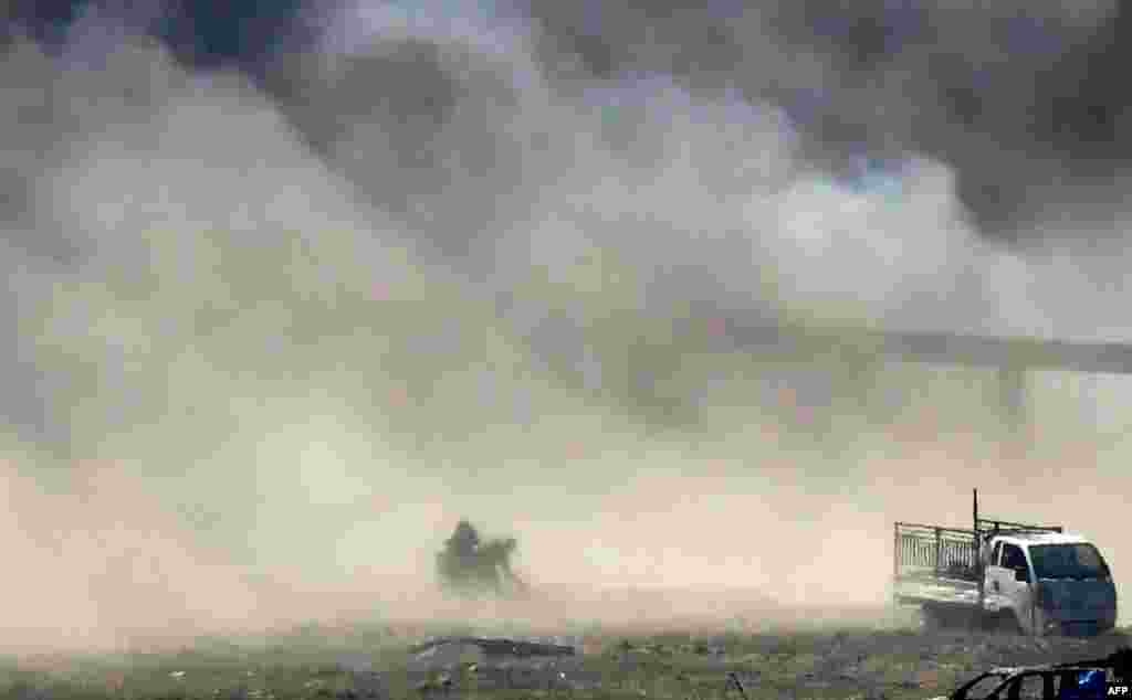 People are seen fleeing as heavy smoke rises above the Islamic State (IS) group&#39;s last remaining position in the village of Baghouz during battles with the Syrian Democratic Forces (SDF), in the countryside of the eastern Syrian province of Deir Ezzor.