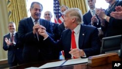 FILE - President Donald Trump gives the pen he used to sign an executive order to Dow Chemical President, Chairman and CEO Andrew Liveris, as other business leaders applaud in the Oval Office of the White House in Washington. Dow Chemical is pushing the Trump administration to scrap the findings of federal scientists who point to a family of widely used pesticides as harmful to about 1,800 critically threatened or endangered species.