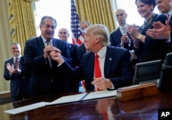 FILE - President Donald Trump gives the pen he used to sign an executive order to Dow Chemical President Andrew Liveris as other business leaders applaud in the Oval Office of the White House in Washington, Feb. 24, 2017. Dow is pushing the Trump administration to scrap the findings of federal scientists who point to a family of widely used pesticides as harmful to about 1,800 threatened or endangered species.