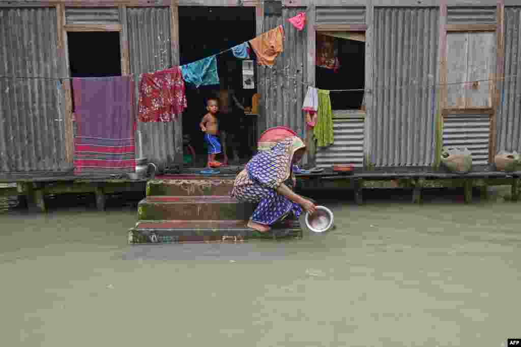 A woman washes her cooking pot in the flood waters outside her house in Sreenagar, Bangladesh.