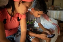 Samuel Andrés Mendoza revisa su cuenta de Twitter, donde vende sus dibujos, con su madre Magdalena Rodríguez en su casa de Barquisimeto, Venezuela. Marzo 2, 2021. Foto: AP.