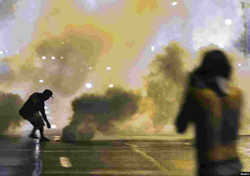 A protester reaches down to throw back a smoke canister as police clear a street after the passing of a midnight curfew meant to stem ongoing demonstrations in reaction to the shooting of Michael Brown in Ferguson, Missouri, Aug. 17, 2014.