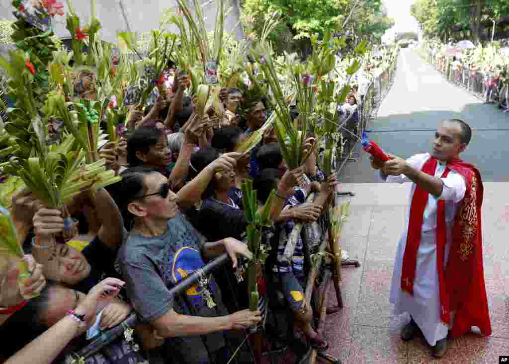 Devotees wave palm fronds as they are blessed by a Roman Catholic priest with holy water in observance of Palm Sunday at Baclaran church in suburban Paranaque city, southeast of Manila, Philippines.