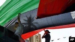 Libyan residents of Jamal Goubtan district in Tripoli hold a giant former Libyan flag for the cars driving under in the streets of Tripoli, Libya, Sept. 1, 2011