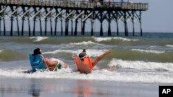 FILE - Vacationers sit in chairs along the surf in Oak Island, N.C., where two youths were hurt in shark attacks on June 14, 2015. 
