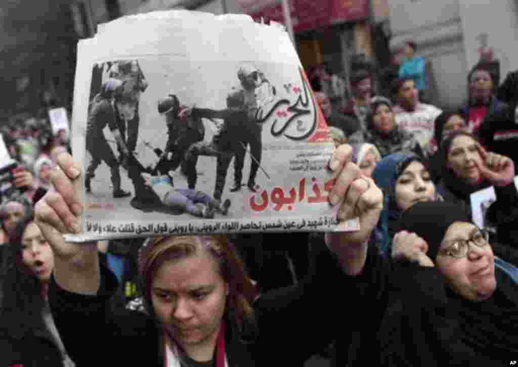 An Egyptian woman raises a copy of Al Tahrir newspaper fronted by a picture showing half naked woman protester beaten by army soldiers as hundreds of Egyptian women march at Cairo streets angered by the recent violence used against them during clashes be