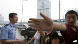 FILE - Plainclothes officer, right, prevents photographer from taking a photo of a Chinese police officer questioning two journalists, Beijing.