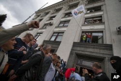 FILE - A Pro-Russian activist waves a Donbas Republic flag over a crowd celebrating the capture of an administration building in the center of Luhansk, Ukraine, April 29, 2014.