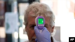 In this June 9, 2020 photo, a patient has his temperature taken with a non-contact infrared thermometer on arrival at Freshney Green Primary Care Center in Grimsby, northeast England.
