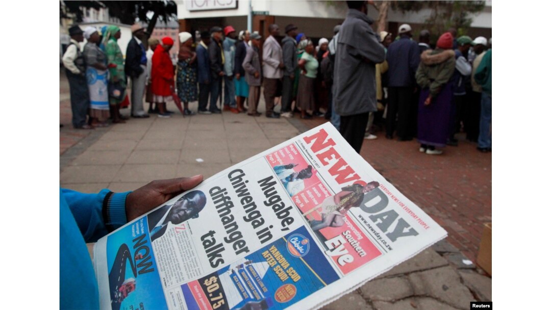 A man reads a newspaper as residents line up to draw money at a bank in Harare, Zimbabwe, Nov. 17, 2017.