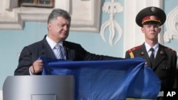 Ukraine's President Petro Poroshenko, left, shows the Ukrainian National flag in front of St. Sophia Cathedral on Ukraine's State Flag Day in Kyiv as he attends the State Flag Day, Aug. 23, 2015.