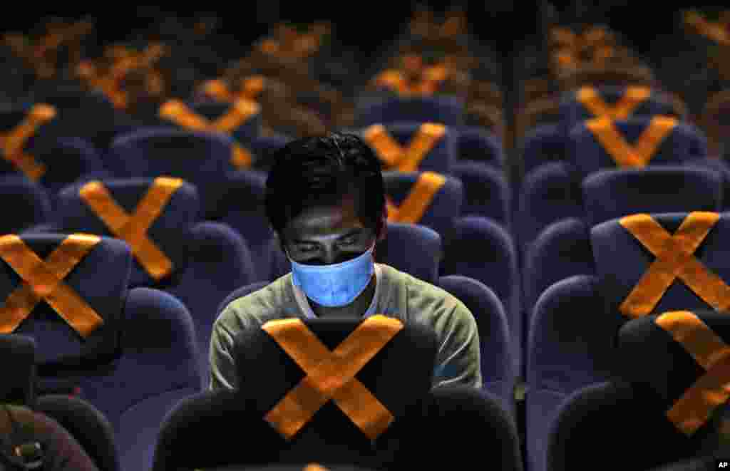 A man checks his mobile phone as he sits amid physical distancing markers prior to the start of a movie at CGV Cinemas theater in Jakarta, Indonesia, Friday, Oct. 23, 2020. The cinema reopened this week after months of closure due to coronavirus outbreak.