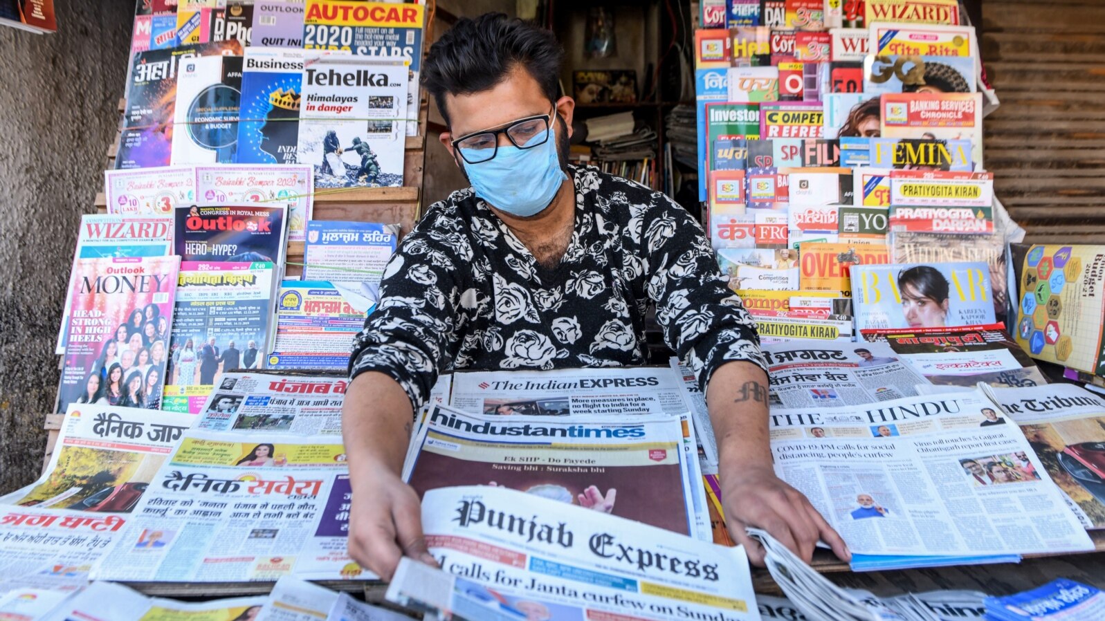 A vendor wearing a facemask amid concerns over the spread of the COVID-19 novel coronavirus, displays newspapers at his stall in Amritsar on March 20, 2020.