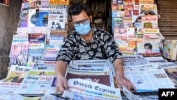 A vendor wearing a facemask amid concerns over the spread of the COVID-19 novel coronavirus, displays newspapers at his stall in Amritsar on March 20, 2020.