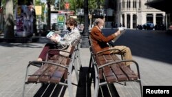 Dos ancianos con mascarillas leen sus periodicos en un parque de Barcelona, España, el 4 de mayo de 2020, tras emitirse un alivio de los confinamientos por el coronavirus.