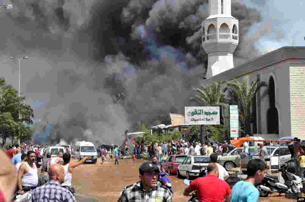 Asap hitam membumbung sementara orang-orang terlihat berkumpul di luar sebuah masjid di lokasi ledakan di kota Tripoli, Lebanon utara. Dua ledakan kuat menewaskan beberapa orang: bom pertama mengguncang pusat kota dekat kediaman mantan Perdana Menteri Najib Mikati, dan yang kedua meledak dekat pelabuhan kota yang sedang bergolak dengan mayoritas Muslim Sunni.