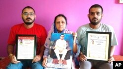 Anindita Mitra, 61, seen with her sons Satyajit Mitra, right and Abhijit Mitra, pose with portraits of her husband, Narayan Mitra, at her house in Silchar, India, Sunday, Sept. 13, 2020. (AP Photo/Joy Roy)