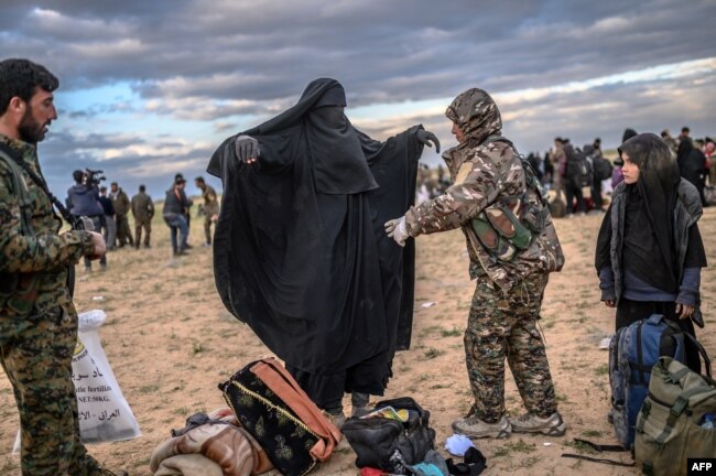 A member of the Kurdish-led Syrian Democratic Forces (SDF) searches a woman after she left the IS group's last holdout of Baghuz, in Syria's northern Deir Ezzor province, Feb. 27, 2019.