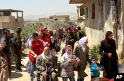 FILE - This photo, released by the Syrian official news agency SANA, shows civilians carrying their belongings leaving towns and villages, in the eastern Ghouta region near Damascus, Syria, March. 25, 2018.