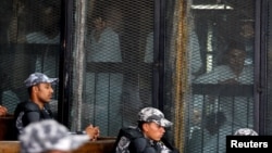 FILE - Police officers sit in the court as suspects are seen behind a fence in Cairo, Egypt, July 28, 2018.