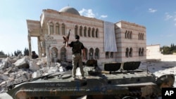 FILE - A Free Syrian Army soldier stands on a Syrian military tank in front of a mosque, which were damaged during fighting with government forces, in the Syrian town of Azaz, on the outskirts of Aleppo, Sept. 23, 2012.