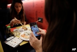 Chiara Valenzano, right, photographs her food as she has lunch with her friend Giulia Terranova at the 'This is not a Sushi bar' restaurant, in Milan, Italy, Oct. 16, 2018. At the restaurant, payment can be made according to the number of Instagram followers one has.