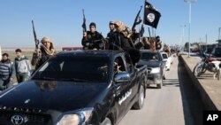 FILE - Islamic State militants pass by a convoy in Tel Abyad town, northeast Syria.