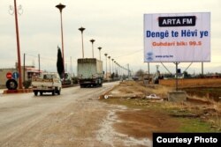 A billboard for one station reads "Your voice is hope" at the entrance of Amude.