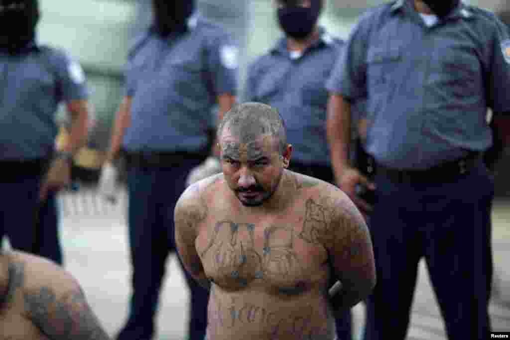 Un miembro de la pandilla Mara Salvatrucha, una de las más grandes y poderosas en El Salvador, espera para ser trasladado a una de las prisiones de máxima seguridad junto a otros reclusos.