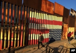 People pass graffiti along the border structure in Tijuana, Mexico, Jan. 25, 2017.