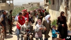 This photo, released by the Syrian official news agency SANA, shows civilians carrying their belongings leaving towns and villages, in the eastern Ghouta region near Damascus, Syria, March. 25, 2018. 