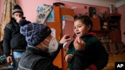 A little girl gets help from Valeriu Nicolae to learn brushing his teeth correctly as her father watches n Nucsoara, Romania, Jan. 9, 2021.