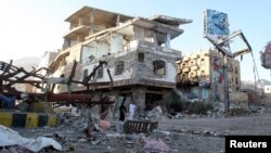 FILE - People walk past a building destroyed during recent fighting in Yemen's southwestern city of Taiz, March 14, 2016. 