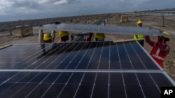 (FILE) Workers install solar panels in the salt desert of Karim Shahi village, in India, on Sept. 21, 2023.