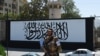 A member of the Taliban's Fateh, a special forces unit, stands guard outside the U.S. embassy in Afghanistan, now with a Taliban flag painted on in its outer concrete wall, in Kabul, Sept. 8, 2021. 