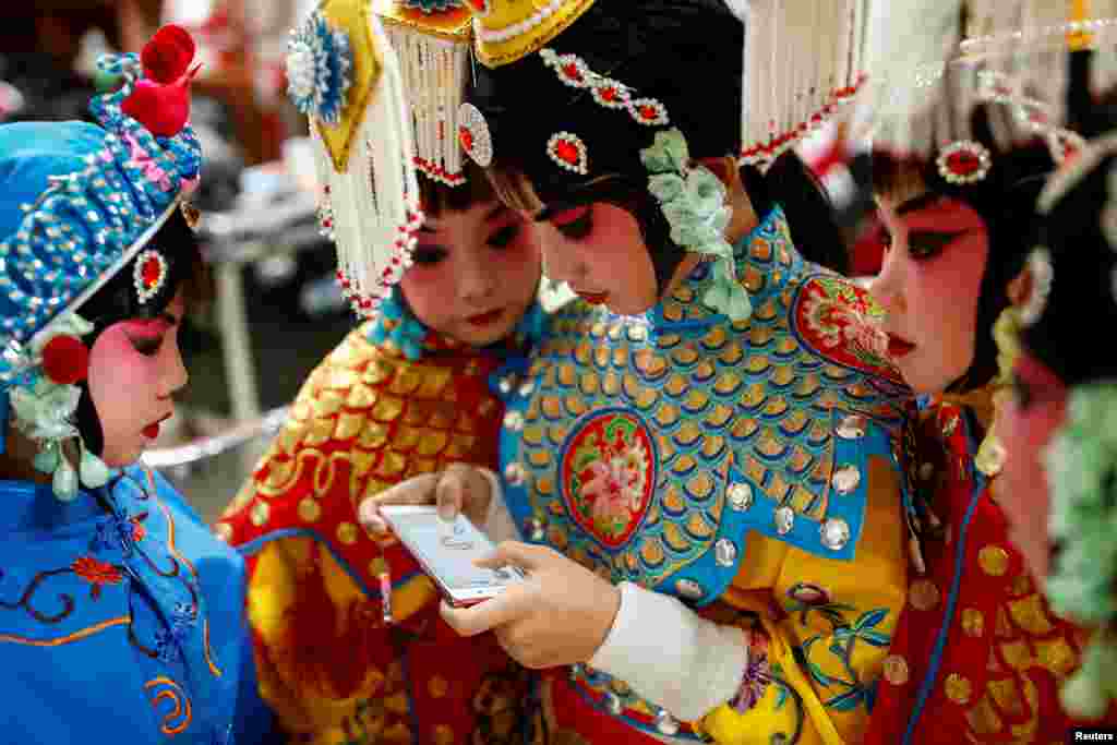 Seorang peserta bermain game dengan ponselnya saat jeda pada kompetisi opera tradisional pada festival seni di Beijing, China.