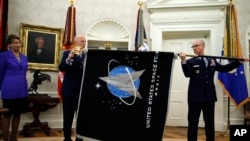 Chief of Space Operations at US Space Force Gen. John Raymond, center, and Chief Master Sgt. Roger Towberman hold the United States Space Force flag as it is presented in the Oval Office of the White House, May 15, 2020.