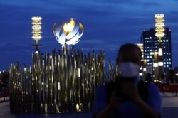 FILE - A man wearing a protective mask stands in front of the second Paralympic flame cauldron at Ariake Yume-no-Ohashi Bridge, a day after the official opening of Tokyo 2020 Paralympic Games, in Tokyo, Japan, Aug. 25, 2021.