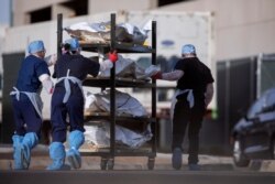 FILE - El Paso County Medical Examiner's Office staff roll bodies in bags labeled "COVID" from refrigerated trailers into the morgue office amid the COVID-19 outbreak, in El Paso, Texas, Nov. 23, 2020.