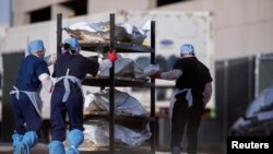 FILE - El Paso County Medical Examiner's Office staff roll bodies that are in bags labeled "Covid" from refrigerated trailers into the morgue office amid the COVID-19 outbreak, in El Paso, Texas, Nov. 23, 2020.