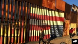 FILE - People pass graffiti along the border structure in Tijuana, Mexico, Jan. 25, 2017. 