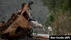 Deux hommes debout au bord de la route, attendant un transport, regardent un camion détruit sur une route menant à la ville d'Abi Adi, dans la région du Tigré, dans le nord de l'Éthiopie, mardi 11 mai 2021. 