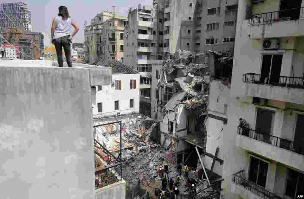 A woman looks on from a rooftop as rescue workers dig through the rubble of a badly damaged building in Lebanon&#39;s capital Beirut, in search of possible survivors from a mega-blast at the adjacent port one month ago, after scanners detected a pulse.