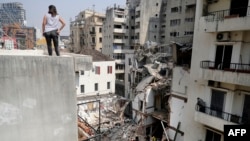 Seorang perempuan dari atap gedung menyaksikan para petugas SAR menyingkirkan puing-puing untuk mencari korban selamat ledakan hebat di kawasan pelabuhan Beirut awal Agustus lalu, Beirut, Lebabon, 4 September 2020. (Foto: AFP)