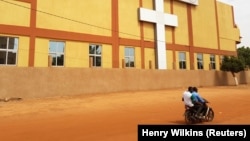 Des gens passent à moto devant une église dans le quartier de Dassasgo à Ouagadougou, au Burkina Faso, le 25 mars 2020. 