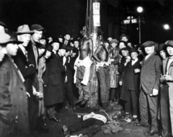 A crowd of white men surround the bodies of Isaac McGhie, Elmer Jackson, and Elias Clayton, who were lynched on June 15, 1920, in Duluth, Minnesota.