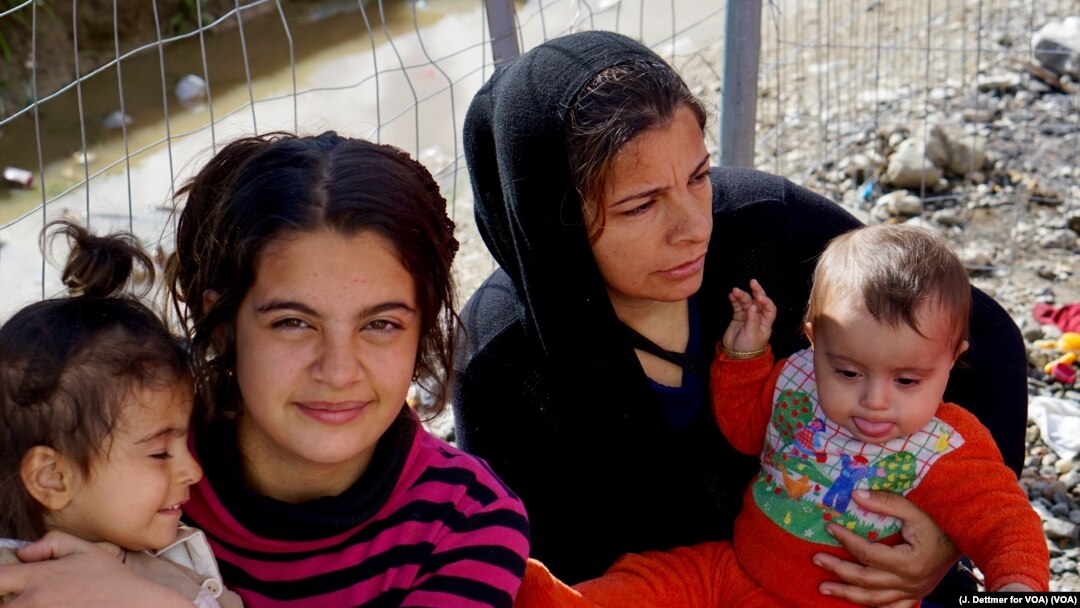Migrant women cradle children near a fence in a makeshift encampment at Greece’s northern border town of Idomeni, March 4, 2016. (J. Dettmer for VOA)