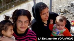 Migrant women cradle children near a fence in a makeshift encampment at Greece’s northern border town of Idomeni, March 4, 2016. (J. Dettmer for VOA)