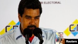 Acting Venezuelan President Nicolas Maduro holds a picture of the late President Hugo Chavez during a news conference at the election commission in Caracas, April 14, 2013. 