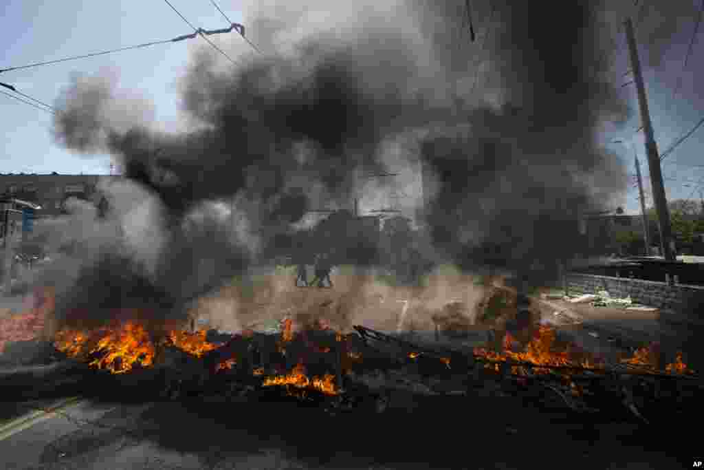 People walk through a square as black smoke billows from burning tires to prevent government armored personnel carriers from passing through the center of Mariupol, eastern Ukraine, May 10, 2014. 